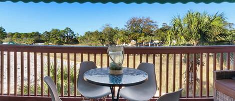 A covered outdoor seating area with a round table and chairs, a decorative glass vase, and a view of the beach and trees.