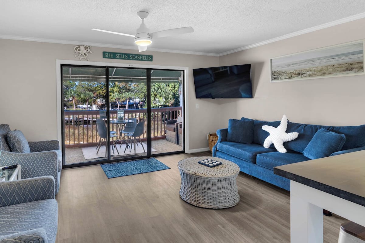 A living room with a blue sofa, a coffee table, and a TV mounted on the wall.