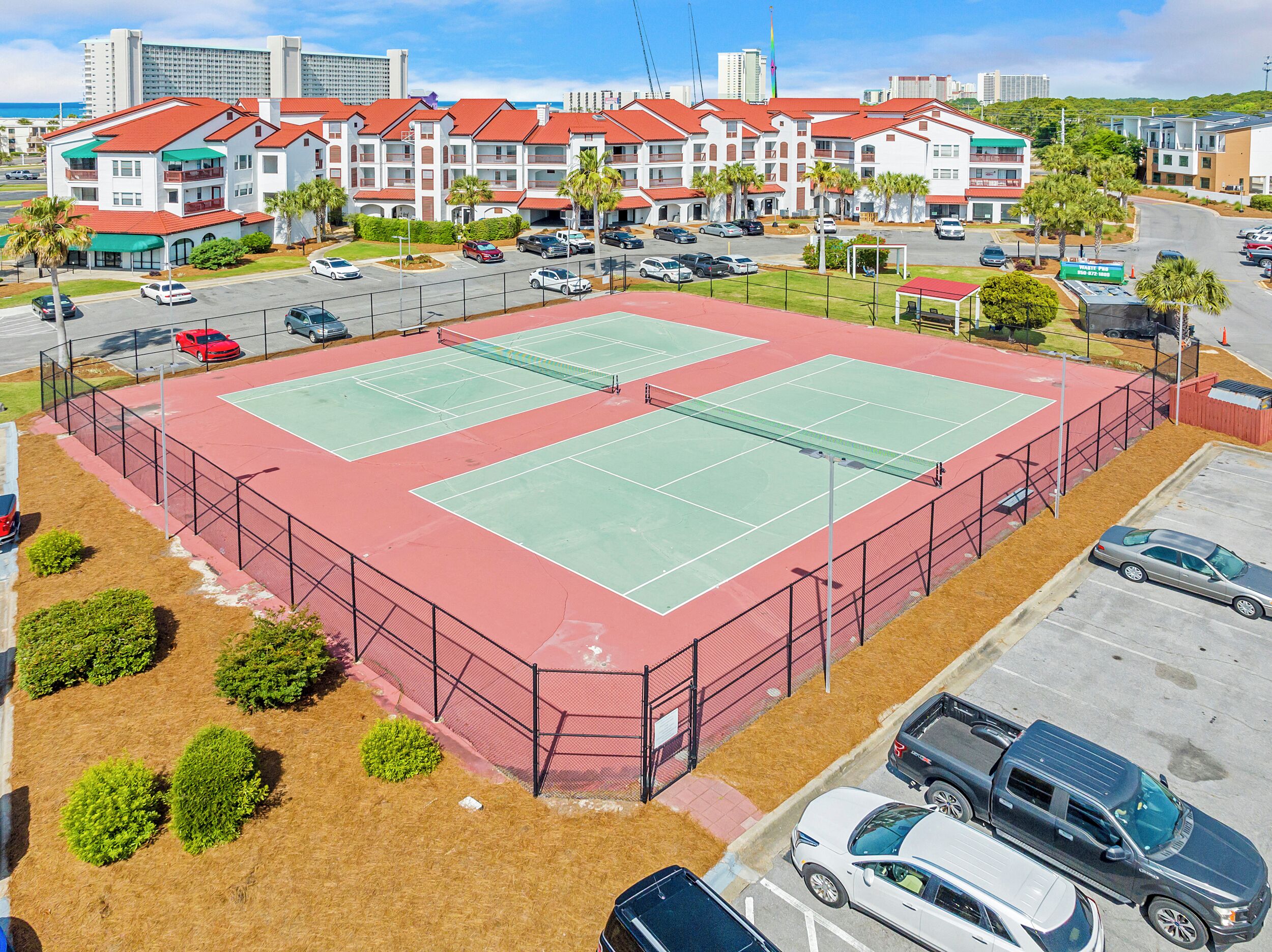 Ein mehrstöckiges Hotel mit roten Dächern und Balkonen, ein Tennisplatz und ein Parkplatz.