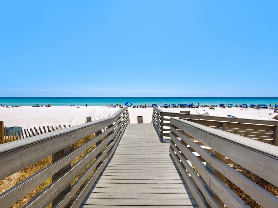 Une promenade en bois qui mène à une plage, avec un ciel dégagé.