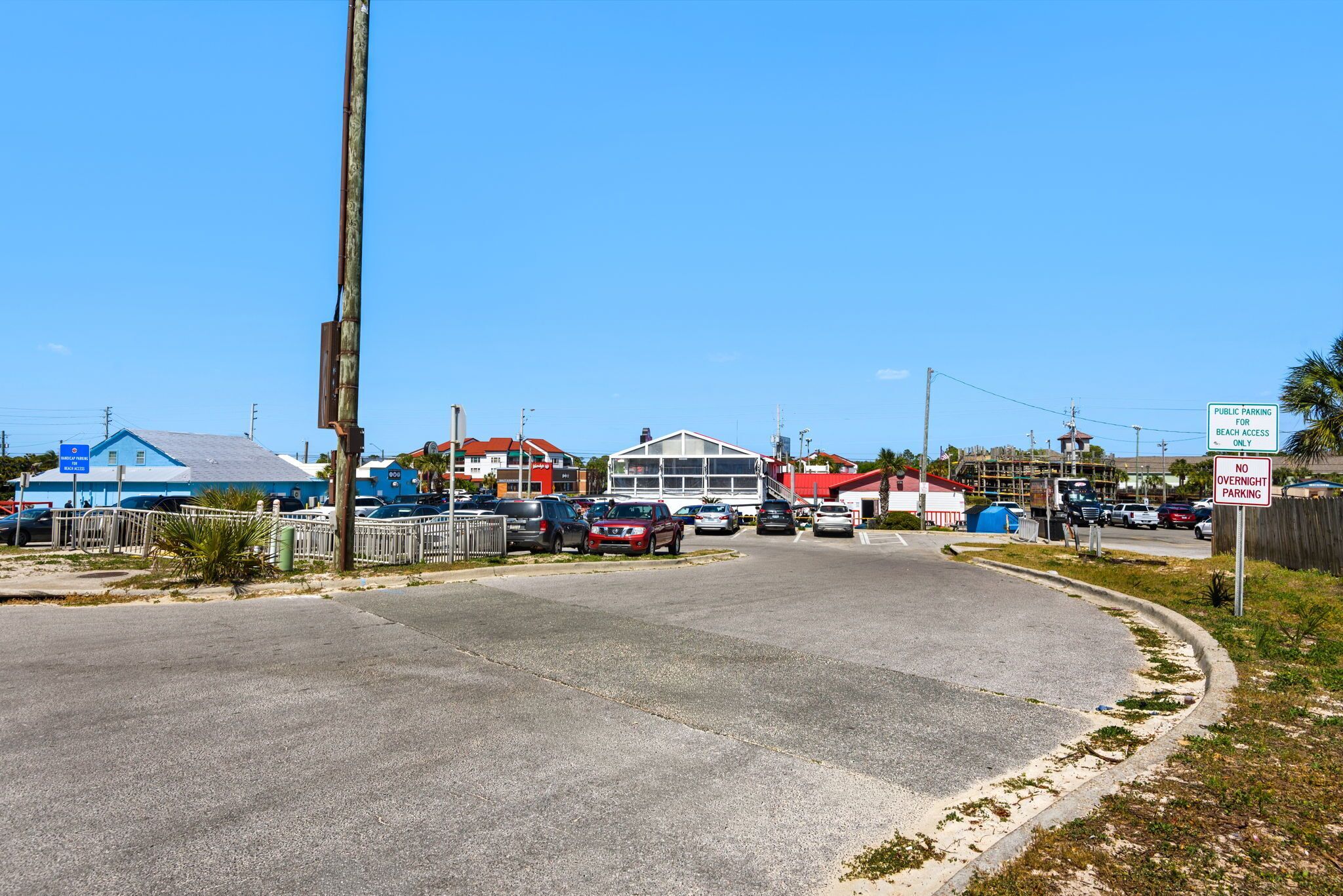 A parking lot with multiple cars, a beach access sign, and a no overnight parking sign.