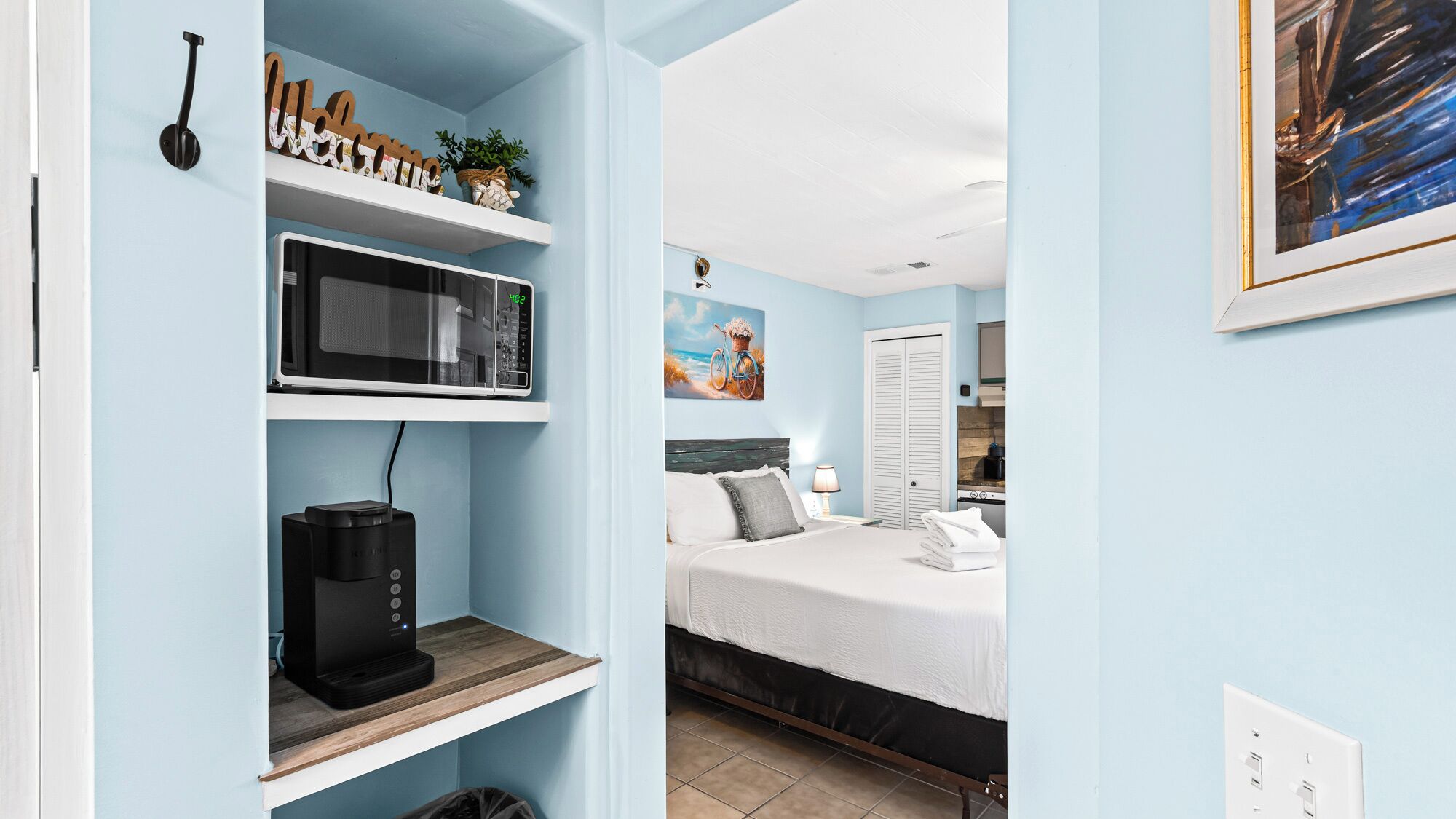 Een kleine slaapkamer met een bed, nachtkastje, magnetron en koffiezetapparaat.