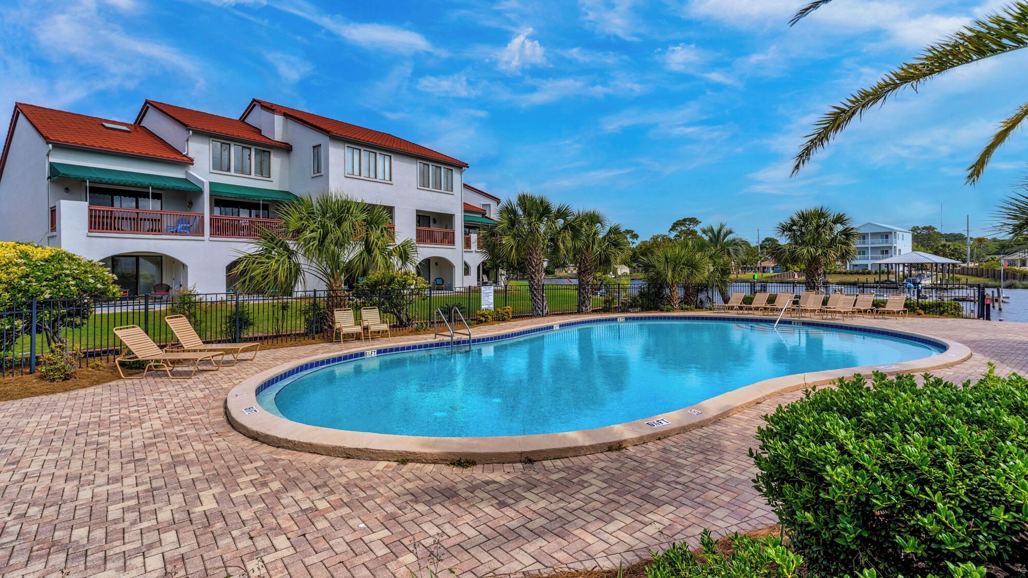 A swimming pool with lounge chairs, a fenced area, and a building with balconies.