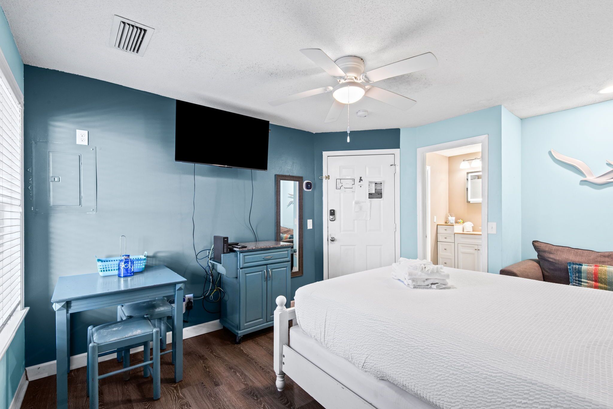 A bedroom with a bed, a desk, a chair, a dresser, a ceiling fan, and a television.