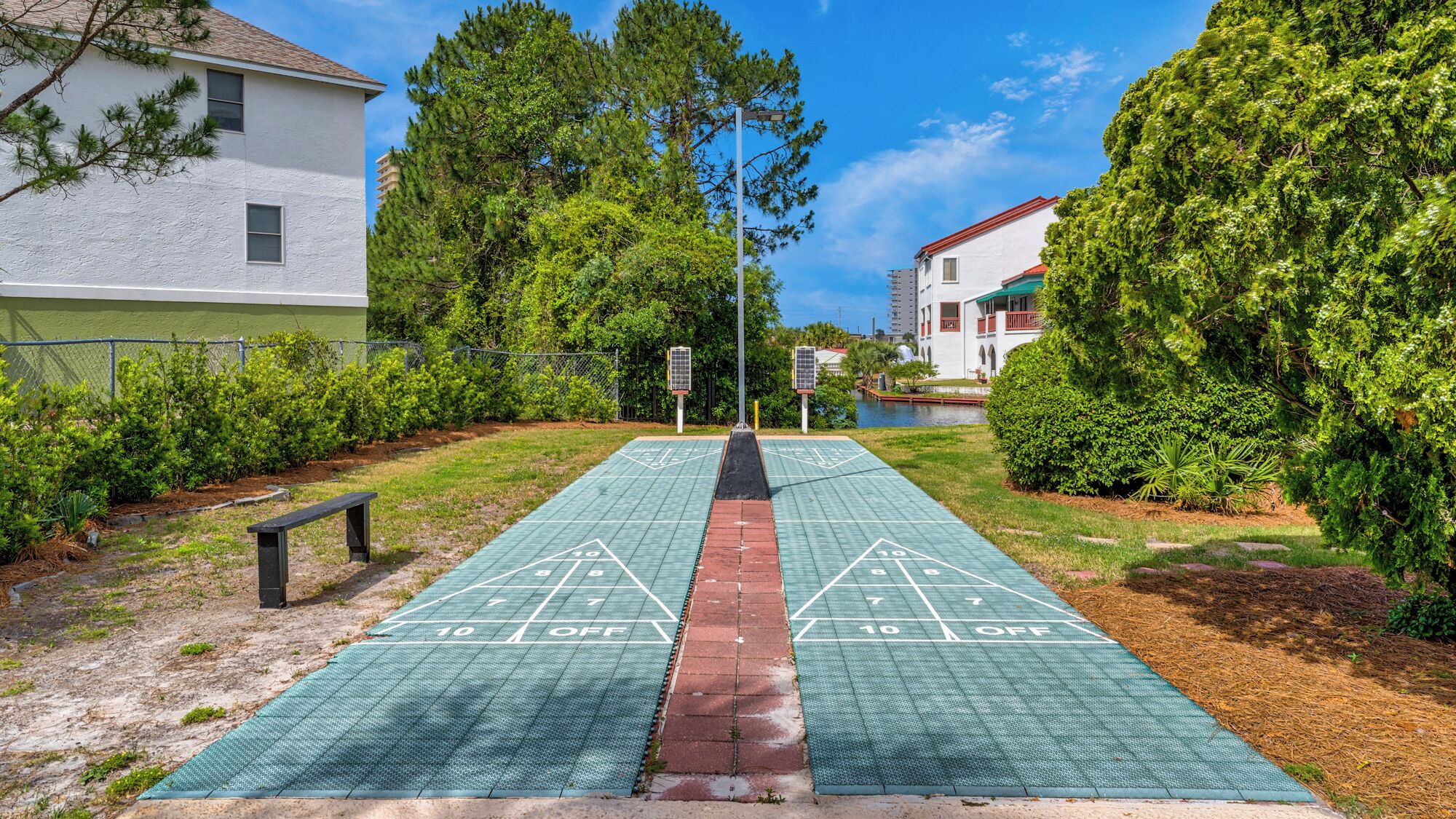 A shuffleboard court with a red divider in the middle, surrounded by greenery and residential buildings.