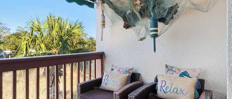 A balcony with wicker furniture and two cushions with the word "Relax" on them.
