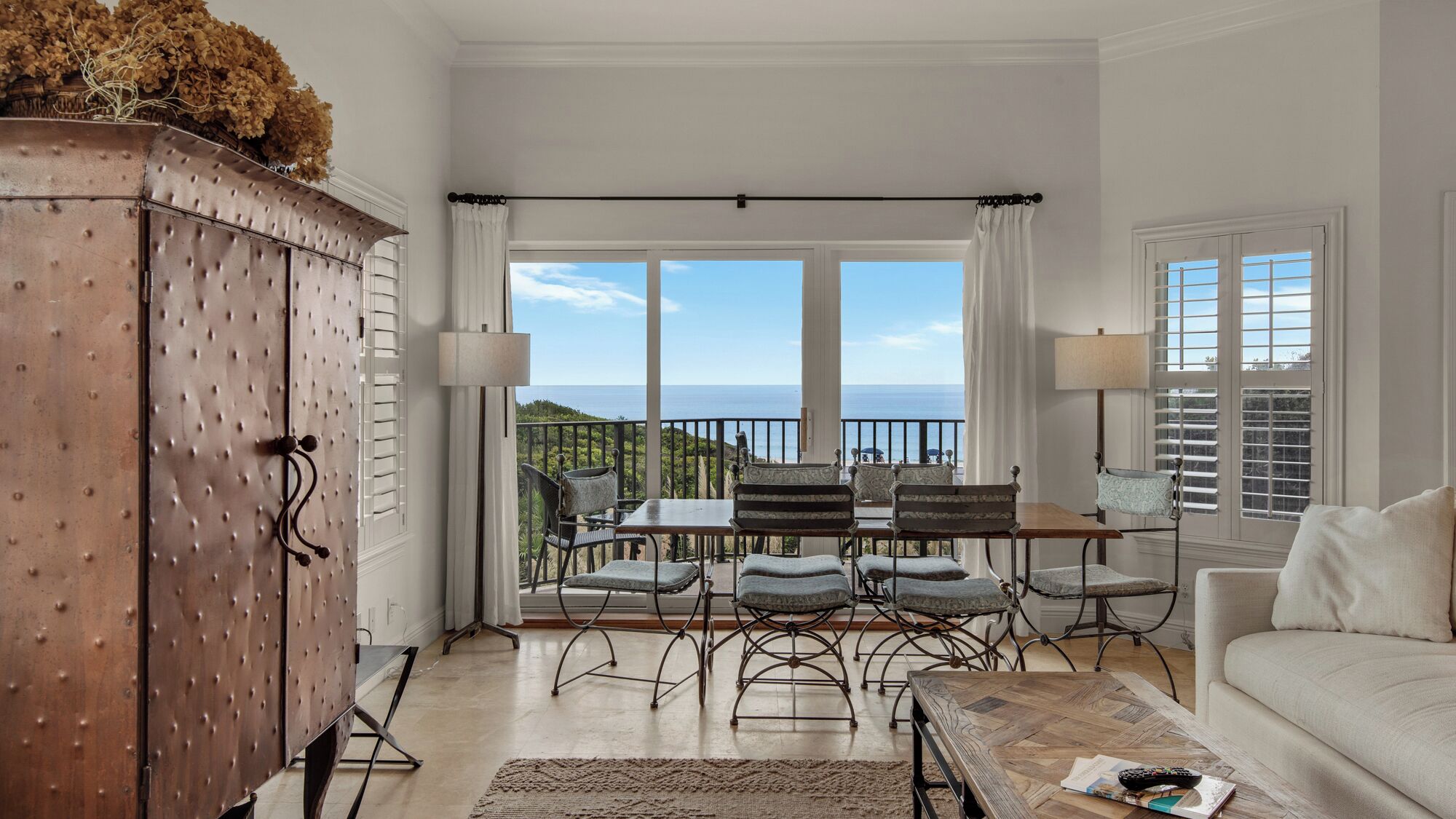 Een ruime woonkamer met een balkon met uitzicht op zee, een houten kast en een witte bank.
