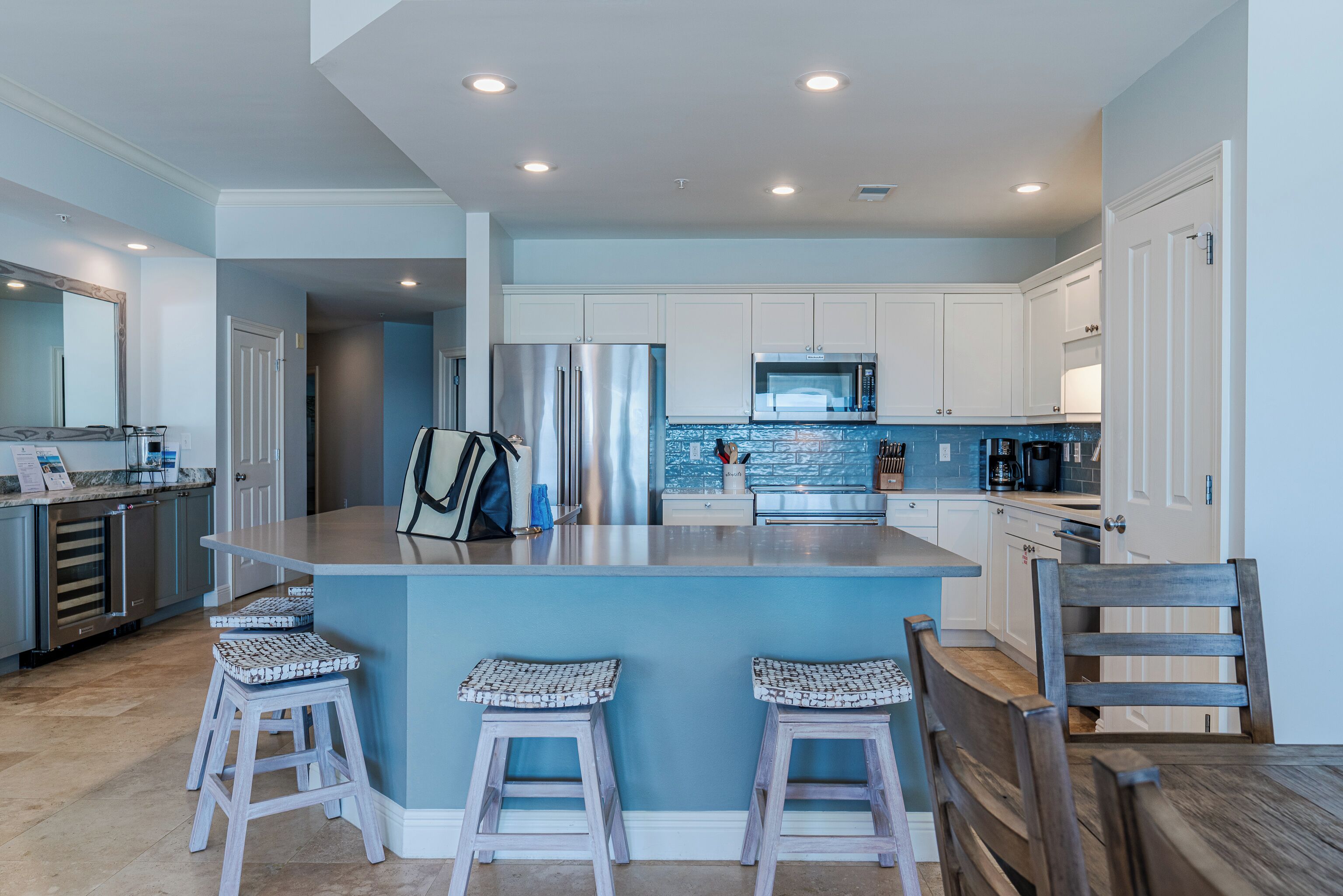Una cocina moderna con gabinetes blancos, electrodomésticos de acero inoxidable y una isla azul con taburetes de bar.