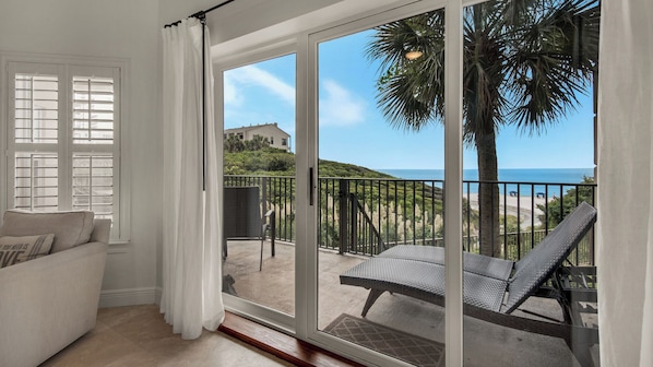 A balcony with a view of the beach, a white sofa, and a dining area with a table and chairs.