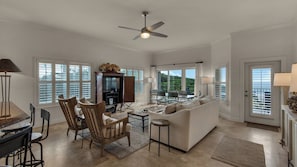 A spacious living room with a large sofa, wooden chairs, a dining table, and a ceiling fan.
