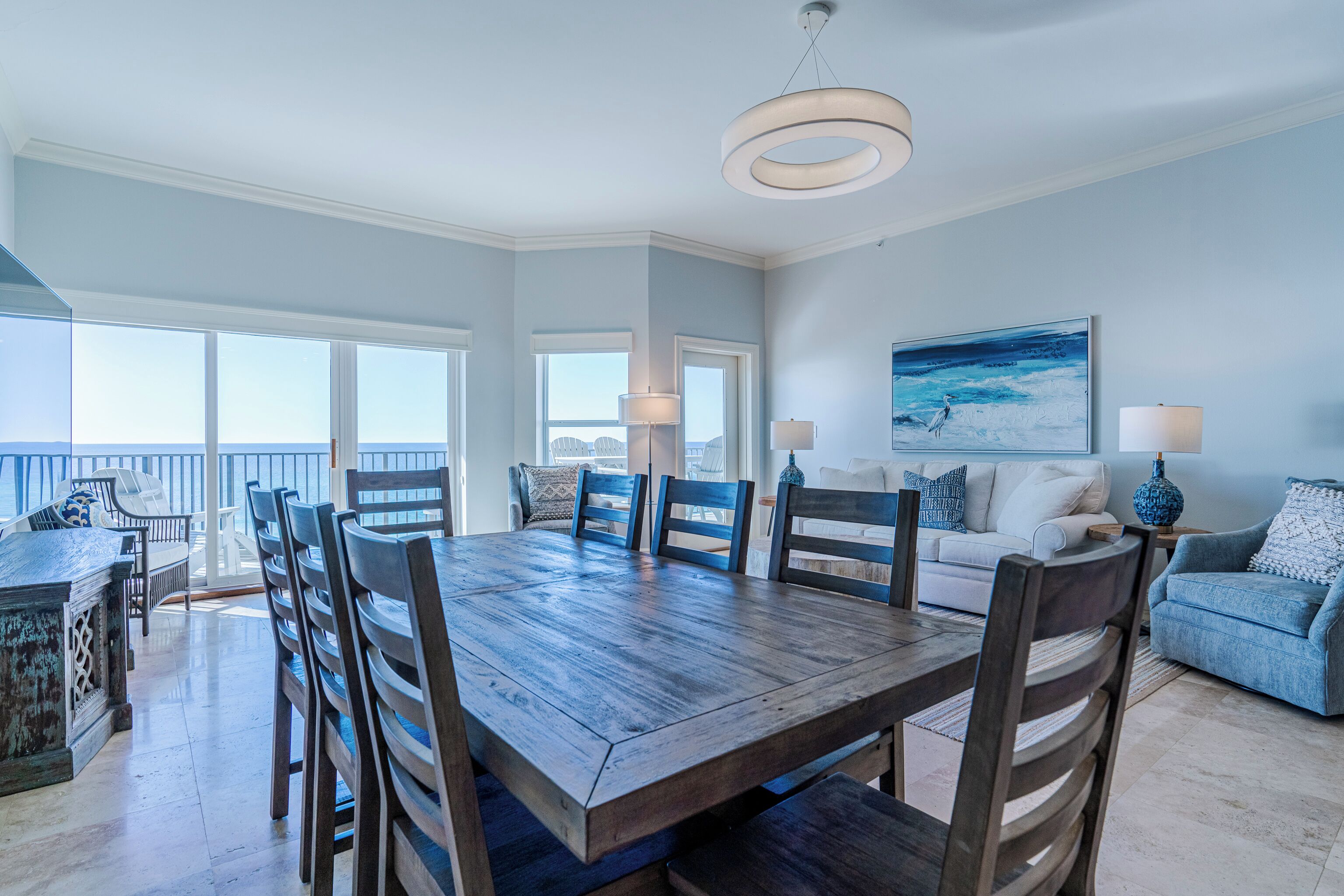 A spacious dining area with a wooden table and chairs, a white sofa, and a view of the ocean.