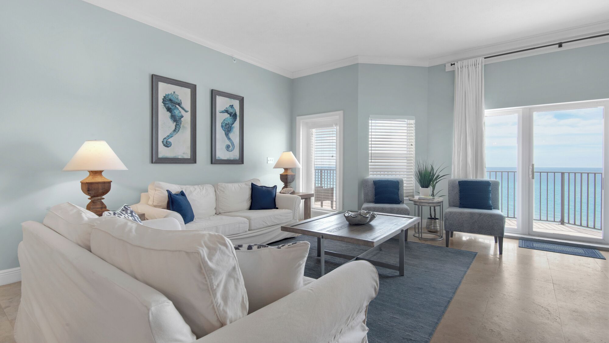 A living room with a white sofa, two armchairs, a coffee table, and a view of the ocean through large windows.