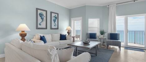 A living room with a white sofa, two armchairs, a coffee table, and a view of the ocean through large windows.