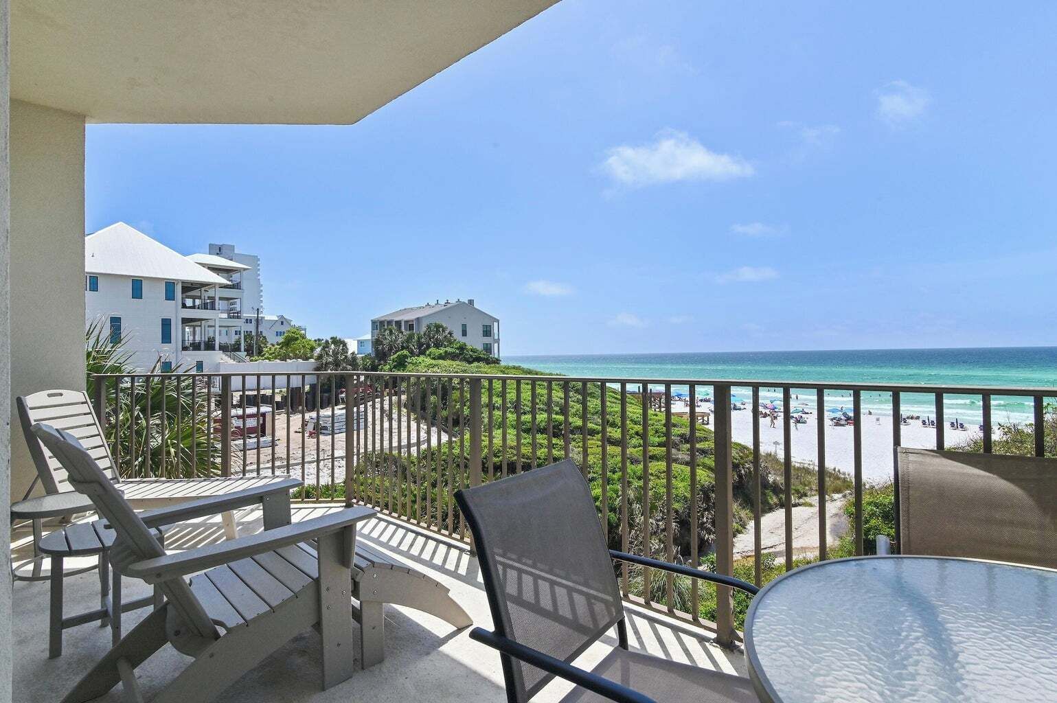 A balcony with a view of the beach and ocean, featuring outdoor seating and a table.