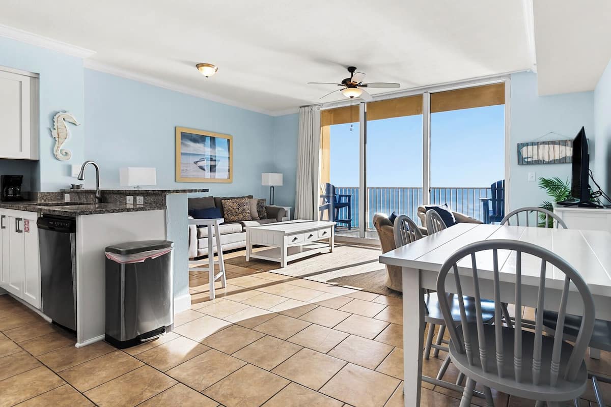 A modern kitchen with a dining area, a balcony with a view, and a ceiling fan.