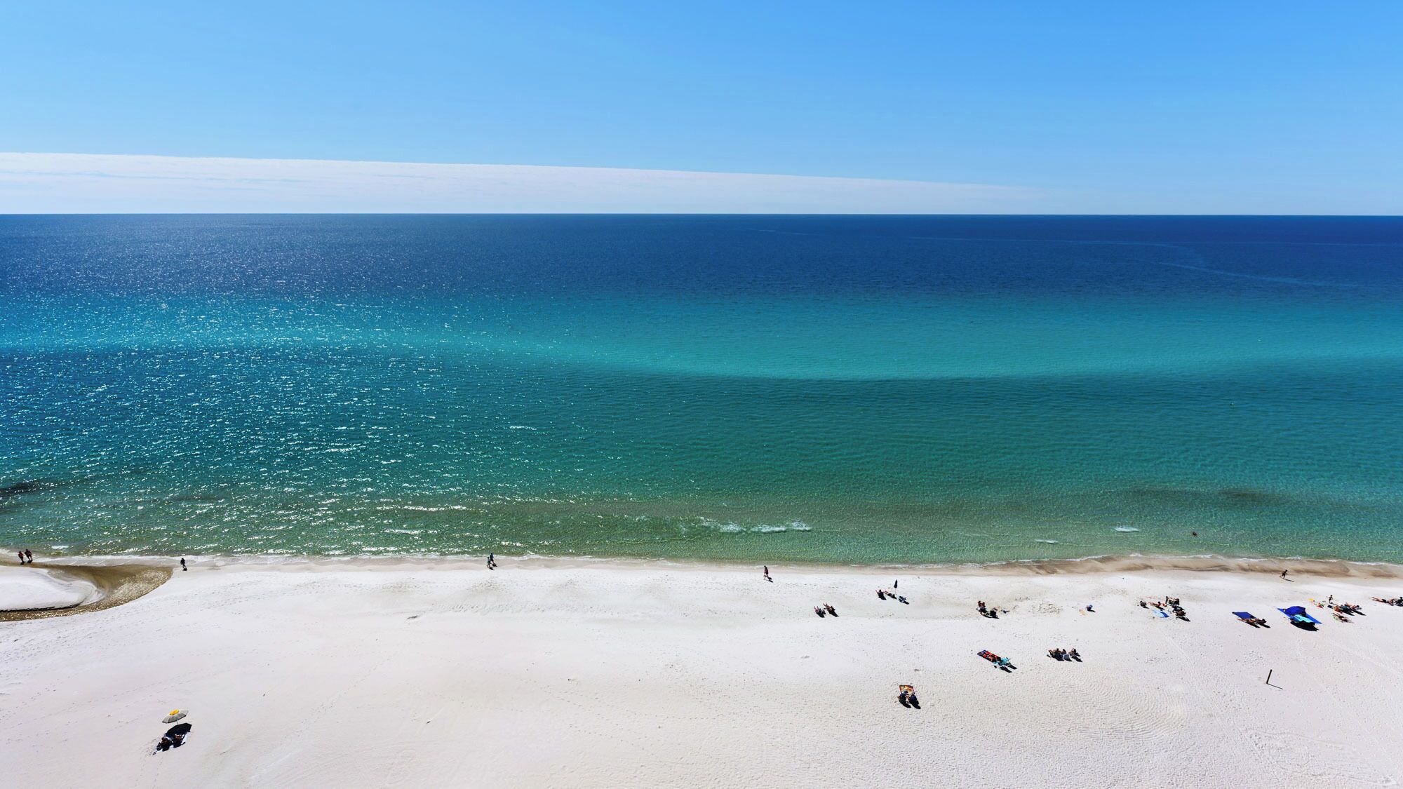 A beach with clear turquoise water and a wide sandy shore.