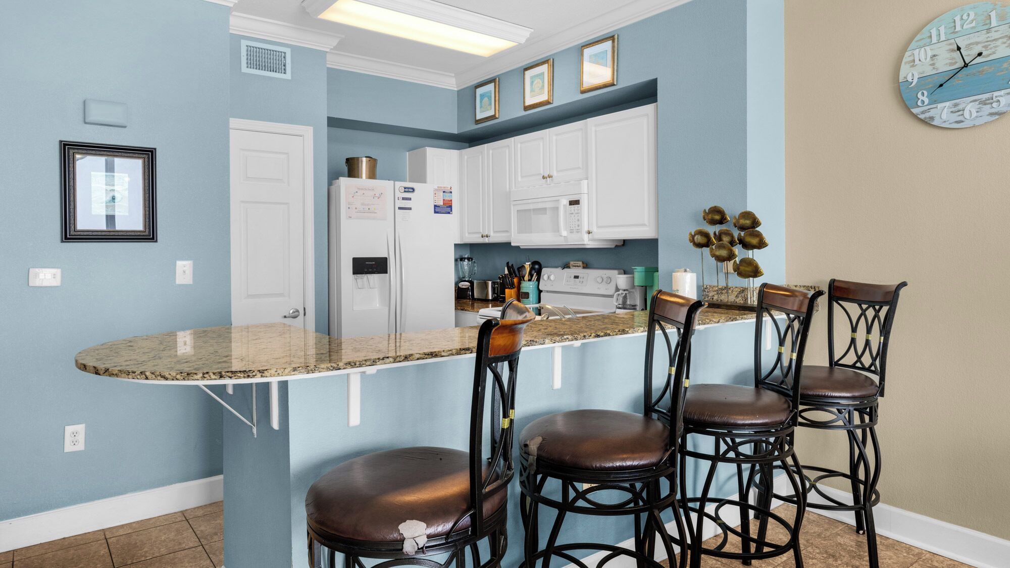 Una cocina con una isla curva, armarios blancos y un reloj en la pared.
