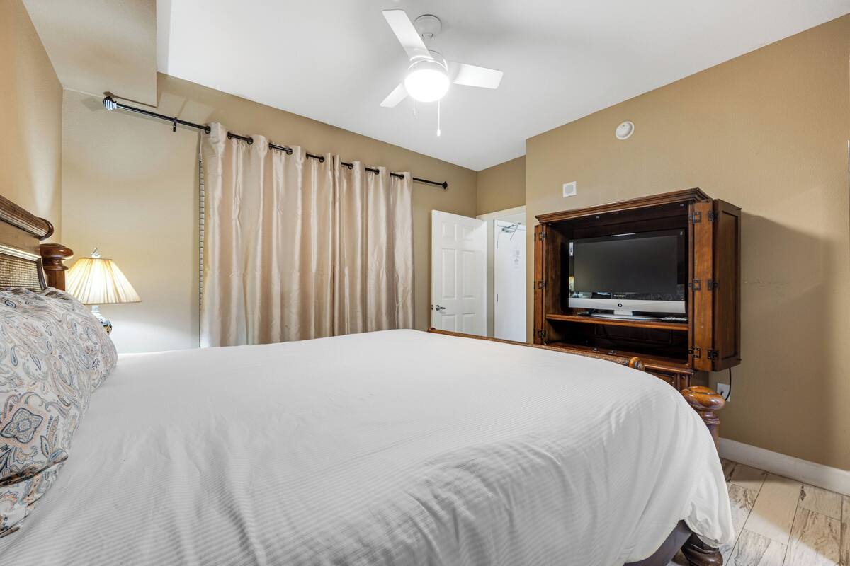 Una habitación de hotel con una cama grande, ventilador de techo, televisión y una puerta.