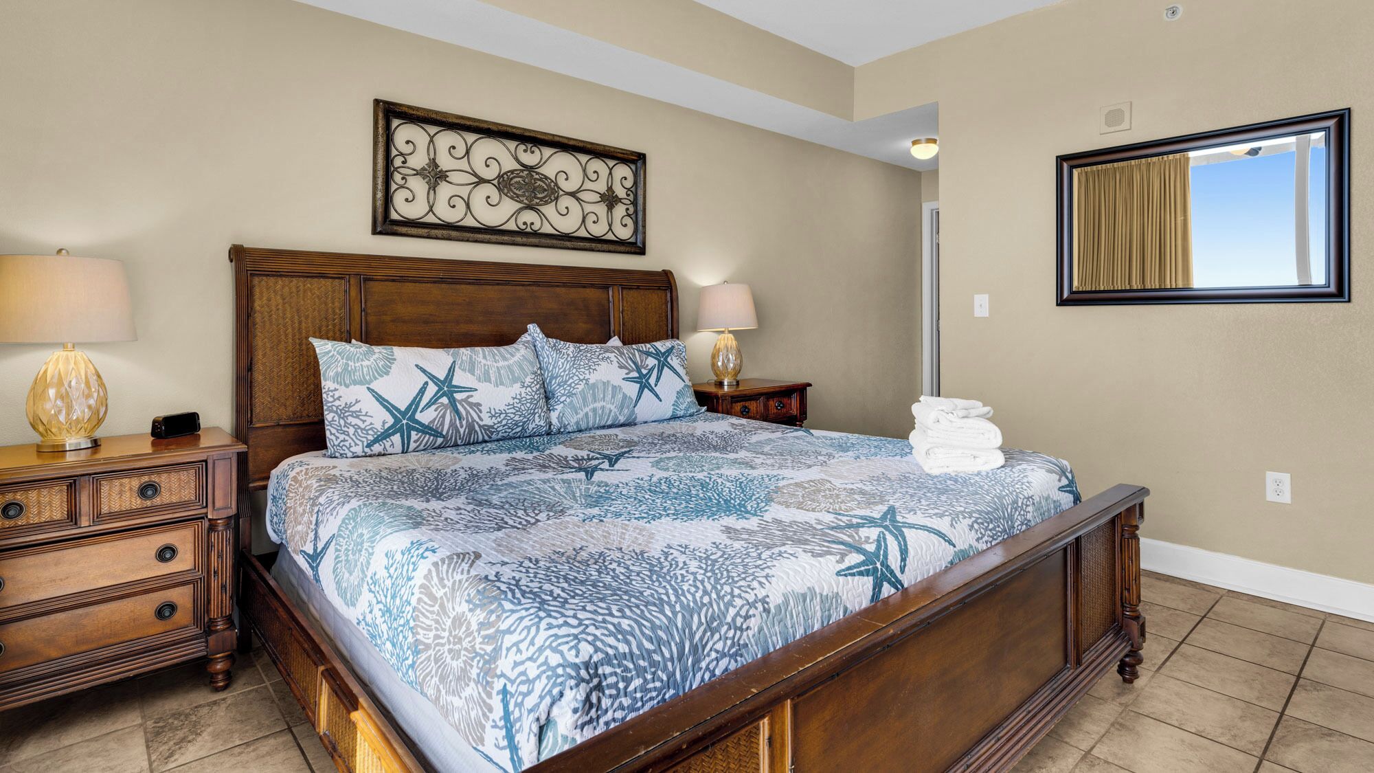 A bedroom with a wooden bed, a nightstand, a lamp, a decorative wall piece, and a window with curtains.