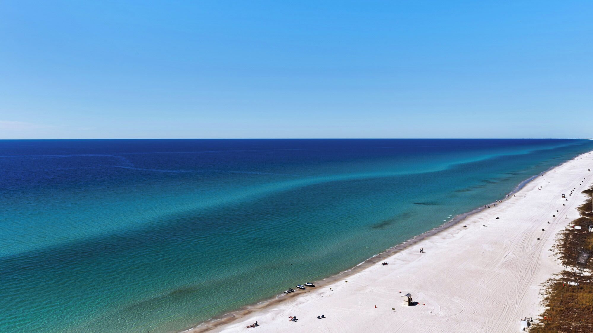 Une plage aux eaux turquoise et limpides, bordée d’une longue étendue de sable blanc.