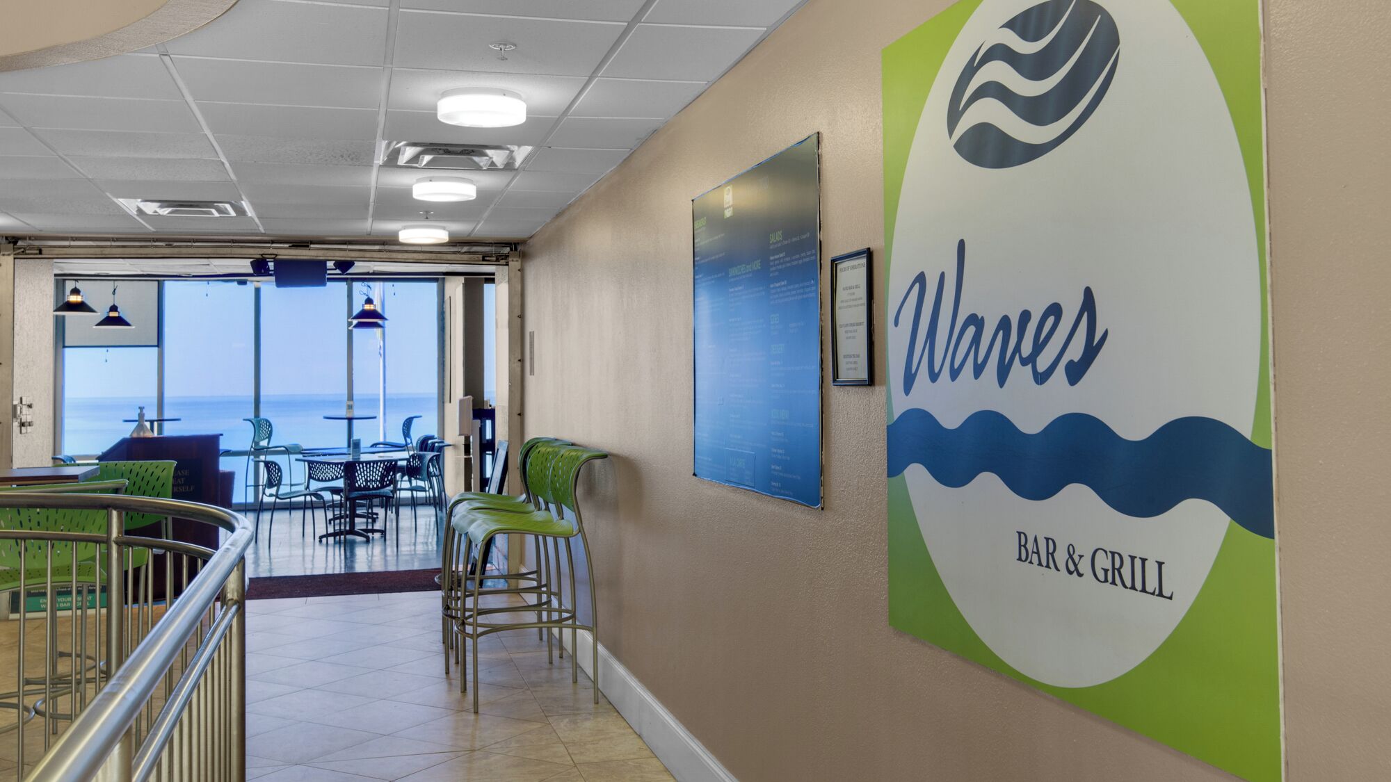 A restaurant interior with a view of the ocean, featuring a sign for 'Waves Bar & Grill' and a menu board.