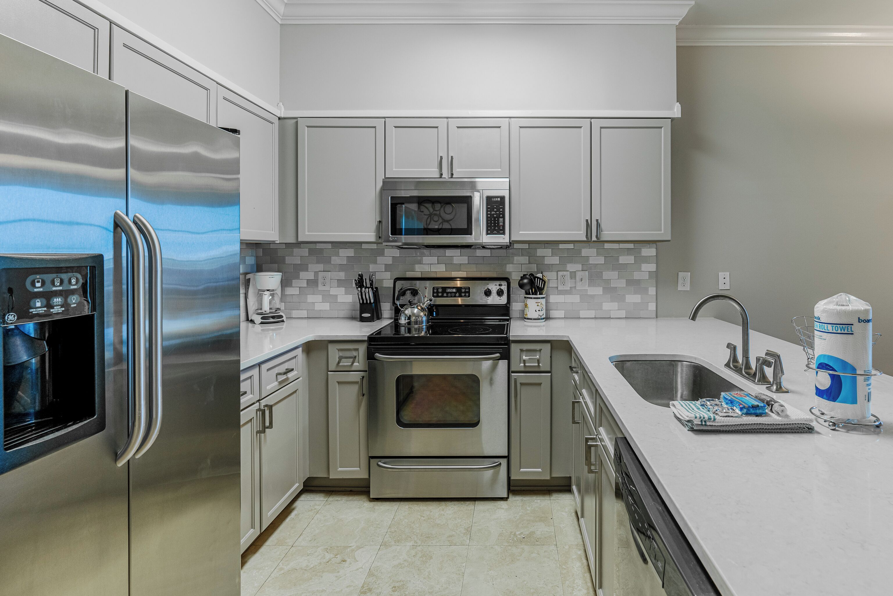 A modern kitchen with stainless steel appliances, white cabinets, and a tiled backsplash.