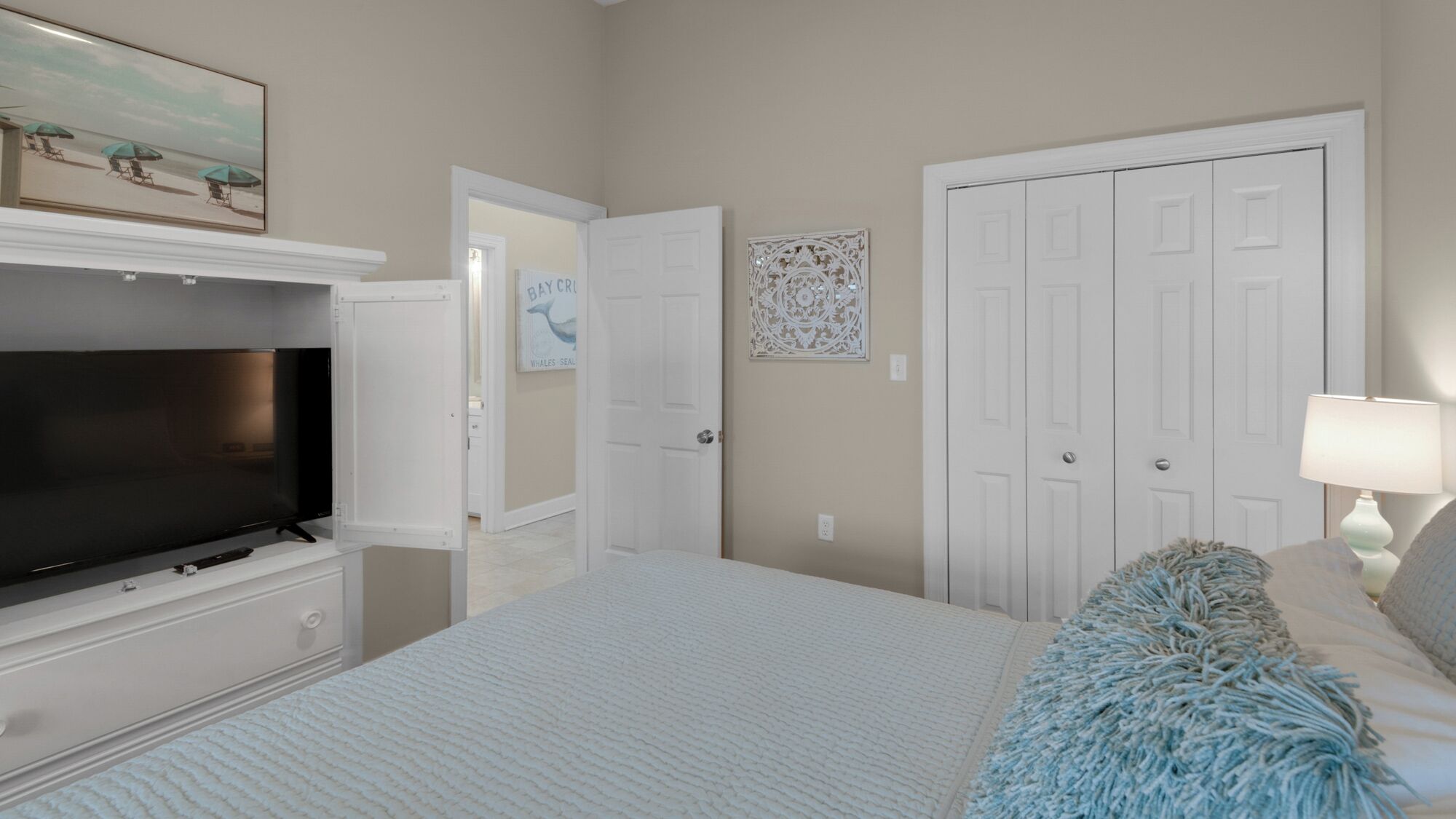 A bedroom with a bed, a television, a wardrobe, and a door leading to another room.