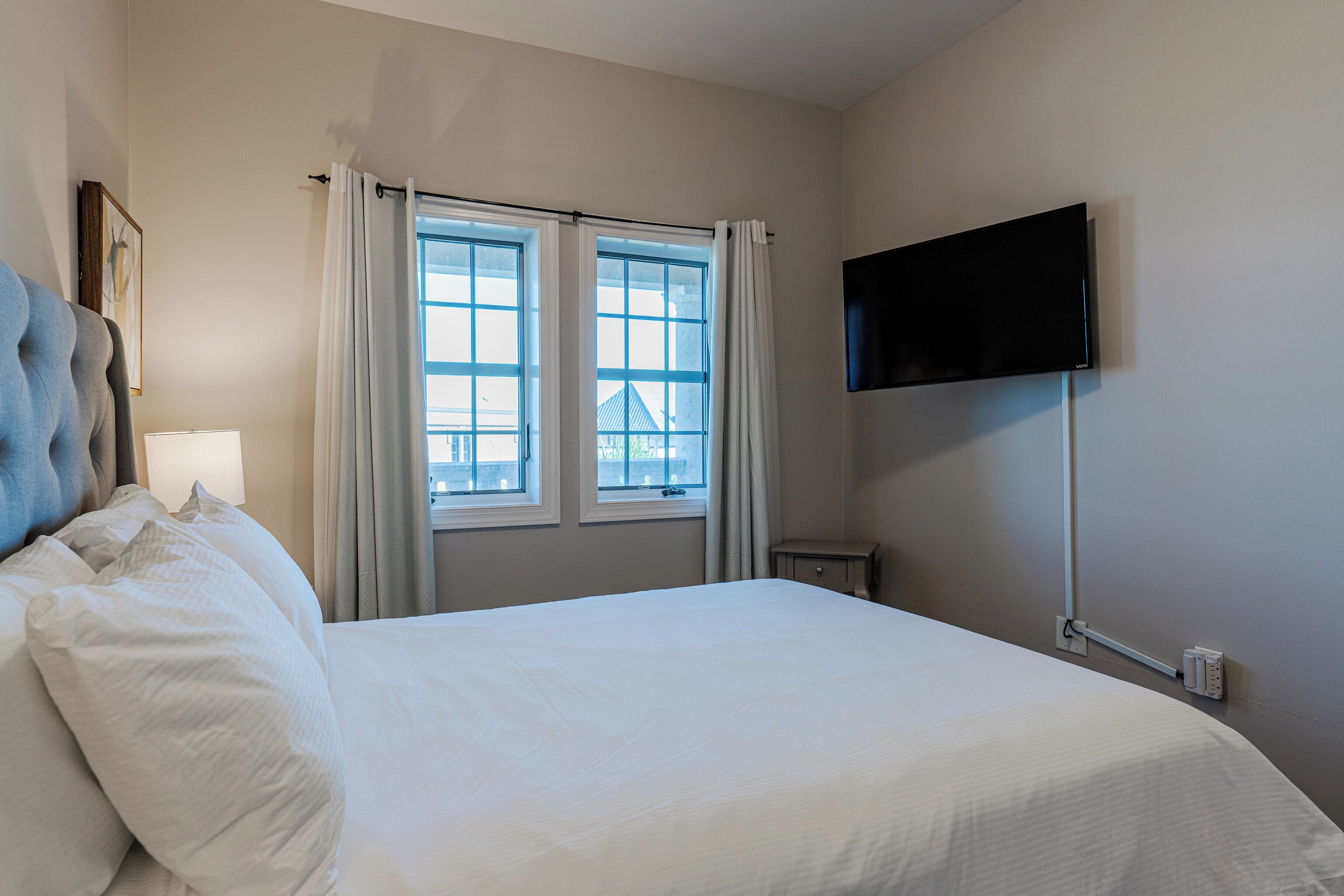 Quarto de hotel com uma cama grande, televisão de tela plana na parede e uma janela com cortinas.