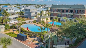 A residential area with a central swimming pool surrounded by houses, palm trees, and a covered outdoor seating area.