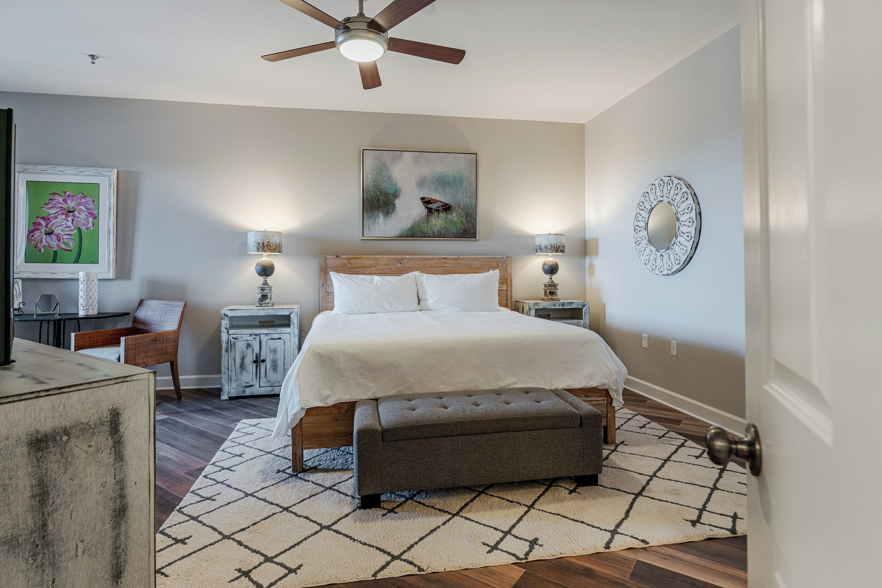 A bedroom with a bed, bedside tables, a ceiling fan, and artwork on the walls.