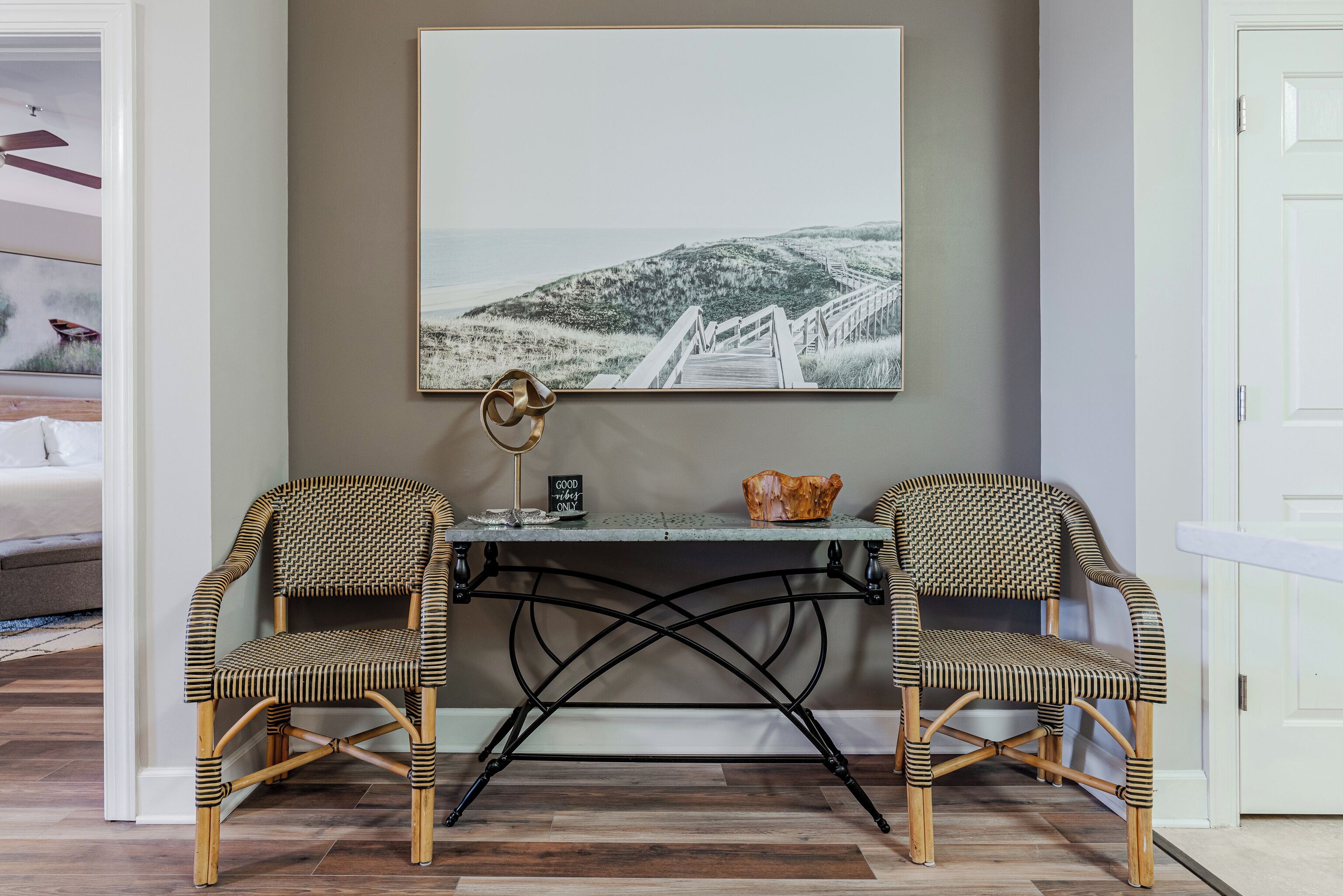A room with a wicker chair and desk, a framed picture on the wall, and a white door.