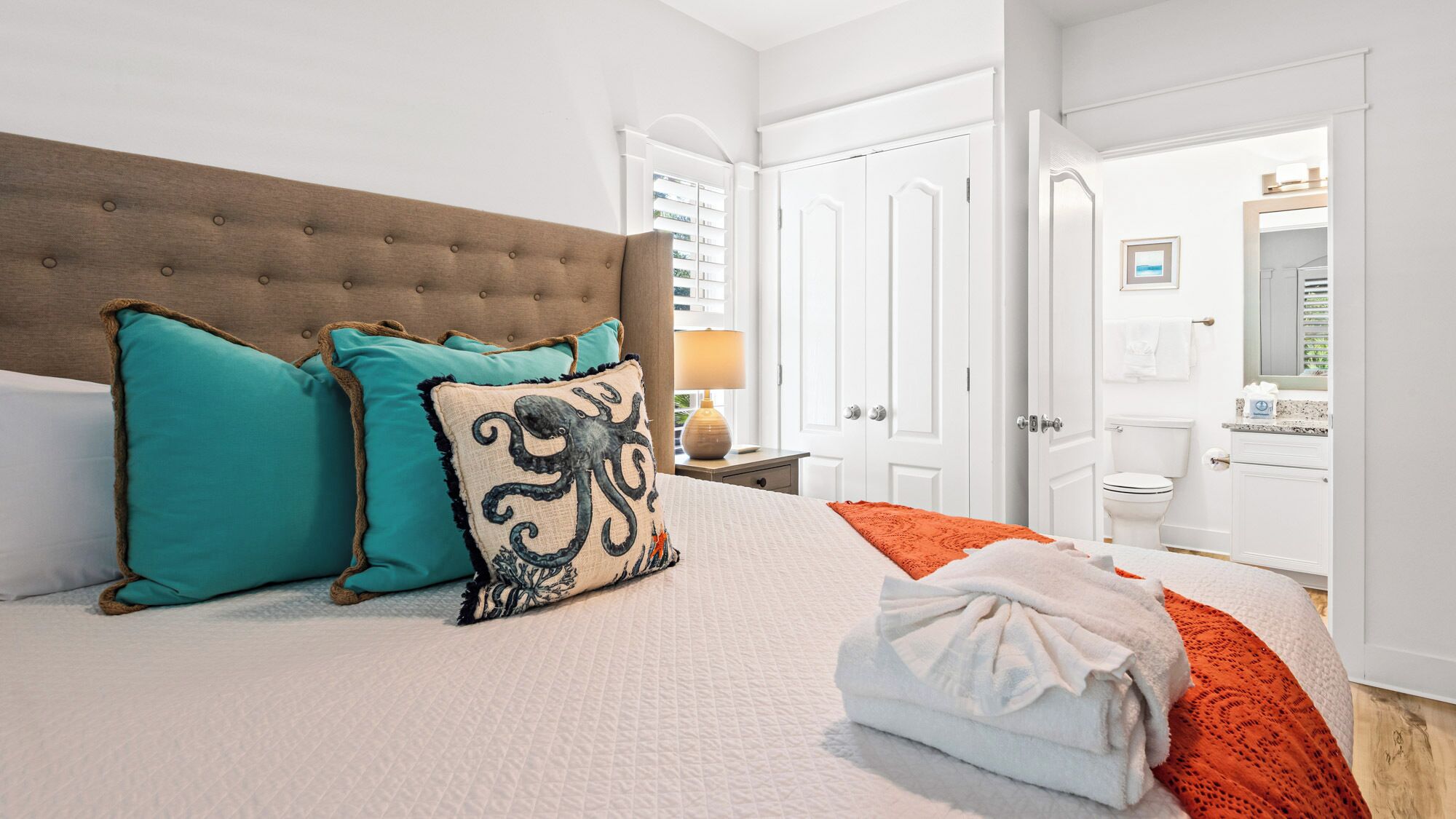 A neatly made bed with a tufted headboard, teal and black patterned pillows, and a folded white towel.