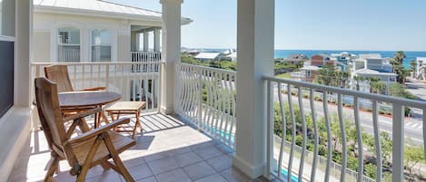 A balcony with a table and chairs, a view of the ocean, and a pool.