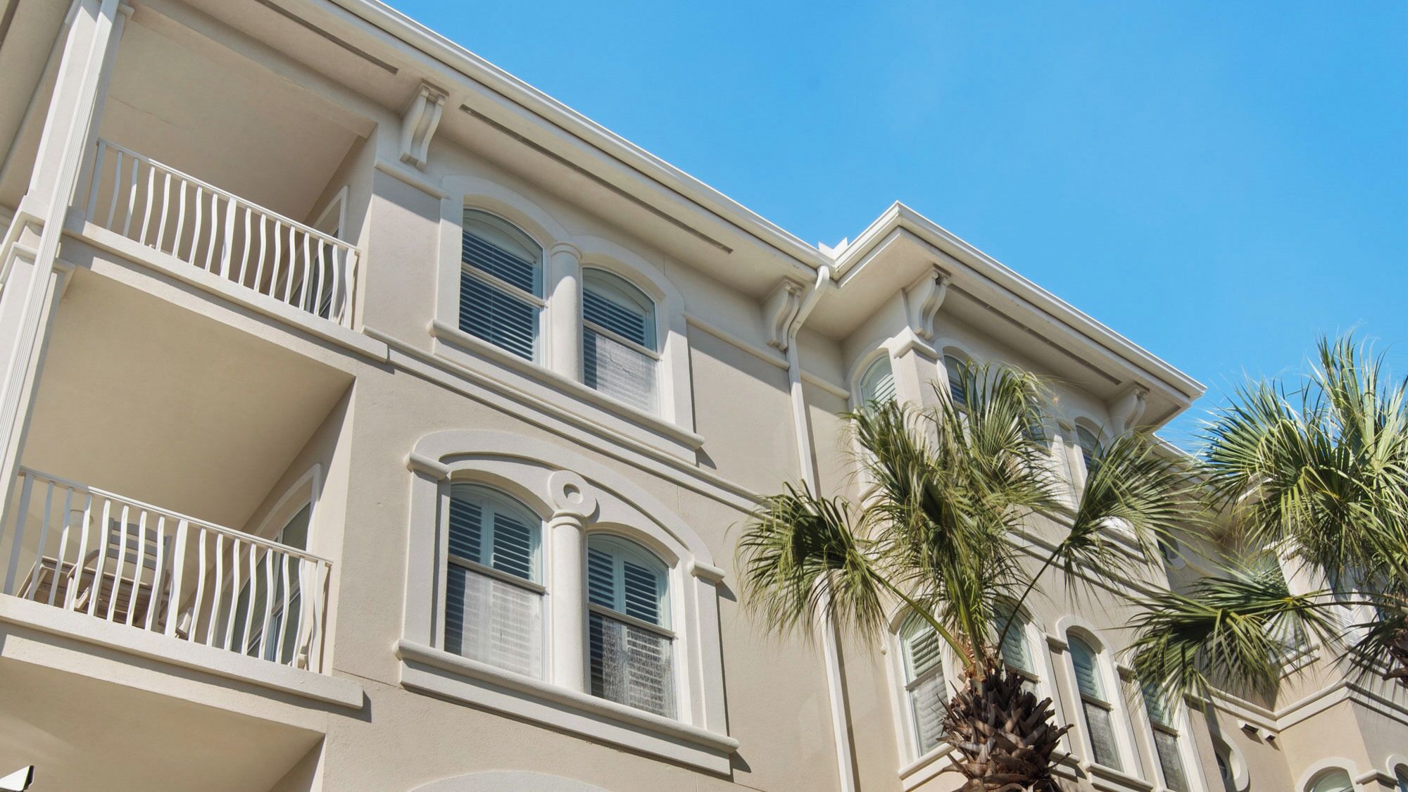 Un immeuble à plusieurs étages doté de balcons, de grandes fenêtres et de palmiers.