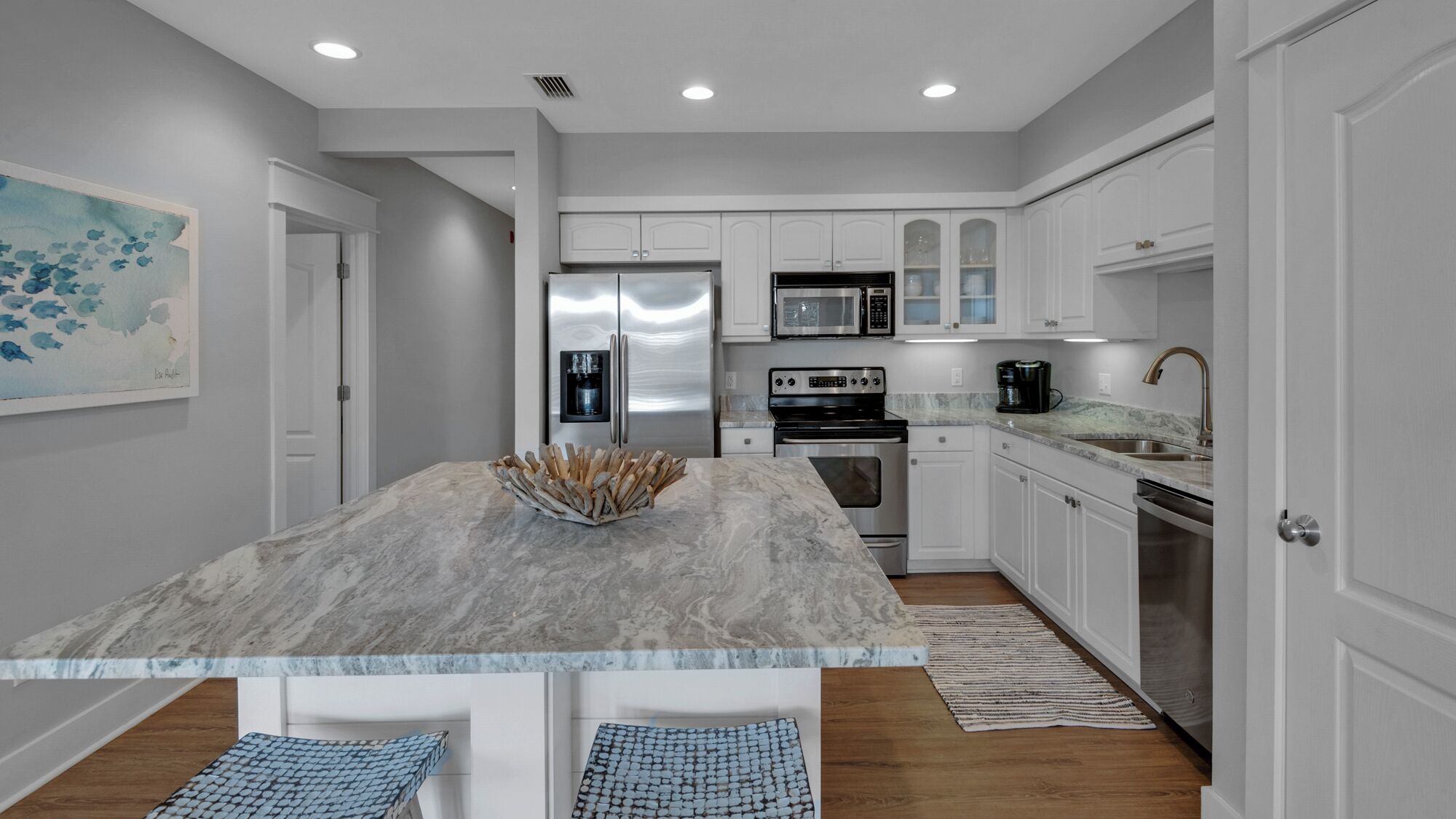 A modern kitchen with white cabinetry, a marble island, stainless steel appliances, and a coffee maker.