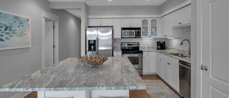 A modern kitchen with white cabinetry, a marble island, stainless steel appliances, and a coffee maker.