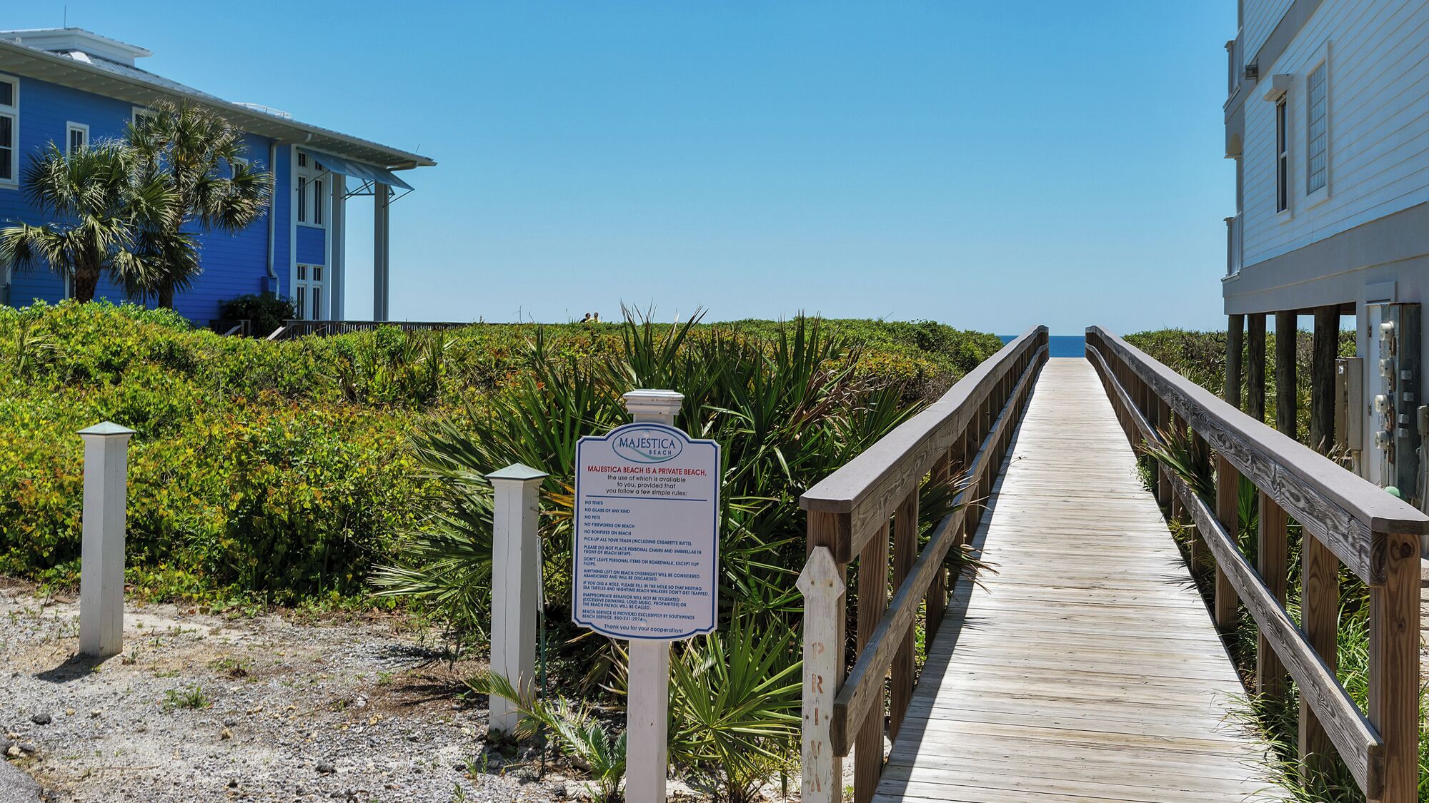 A wooden boardwalk leading to a beach, with a sign indicating it is a private beach with specific rules.
