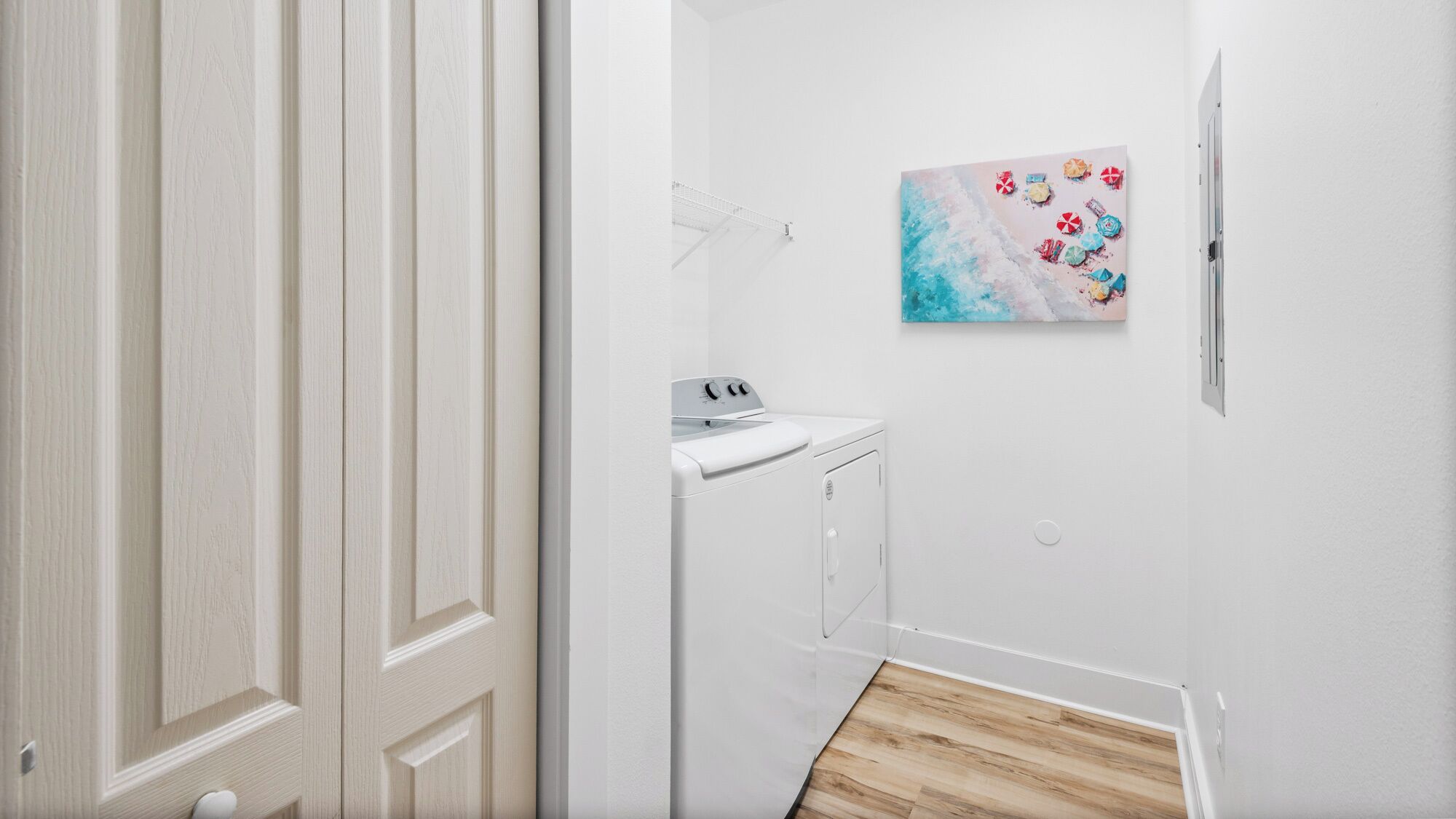 A laundry room with a washing machine and dryer, a painting on the wall, and a wooden floor.