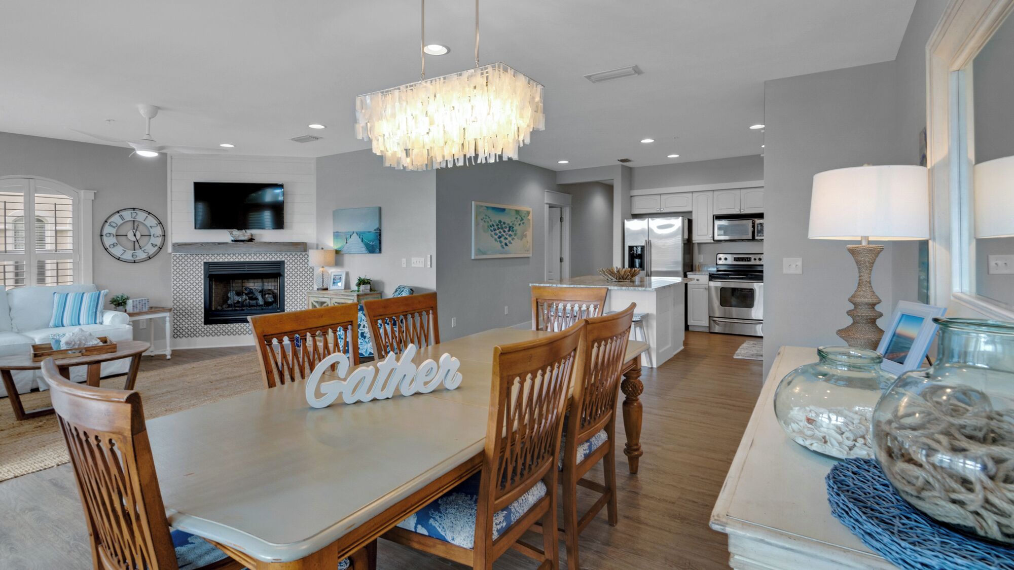 A spacious dining area with a wooden table and chairs, a chandelier, and a kitchen in the background.