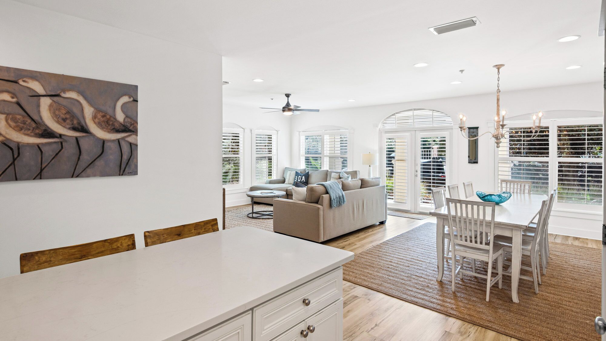 A modern kitchen with a white countertop, wooden chairs, and a dining table.