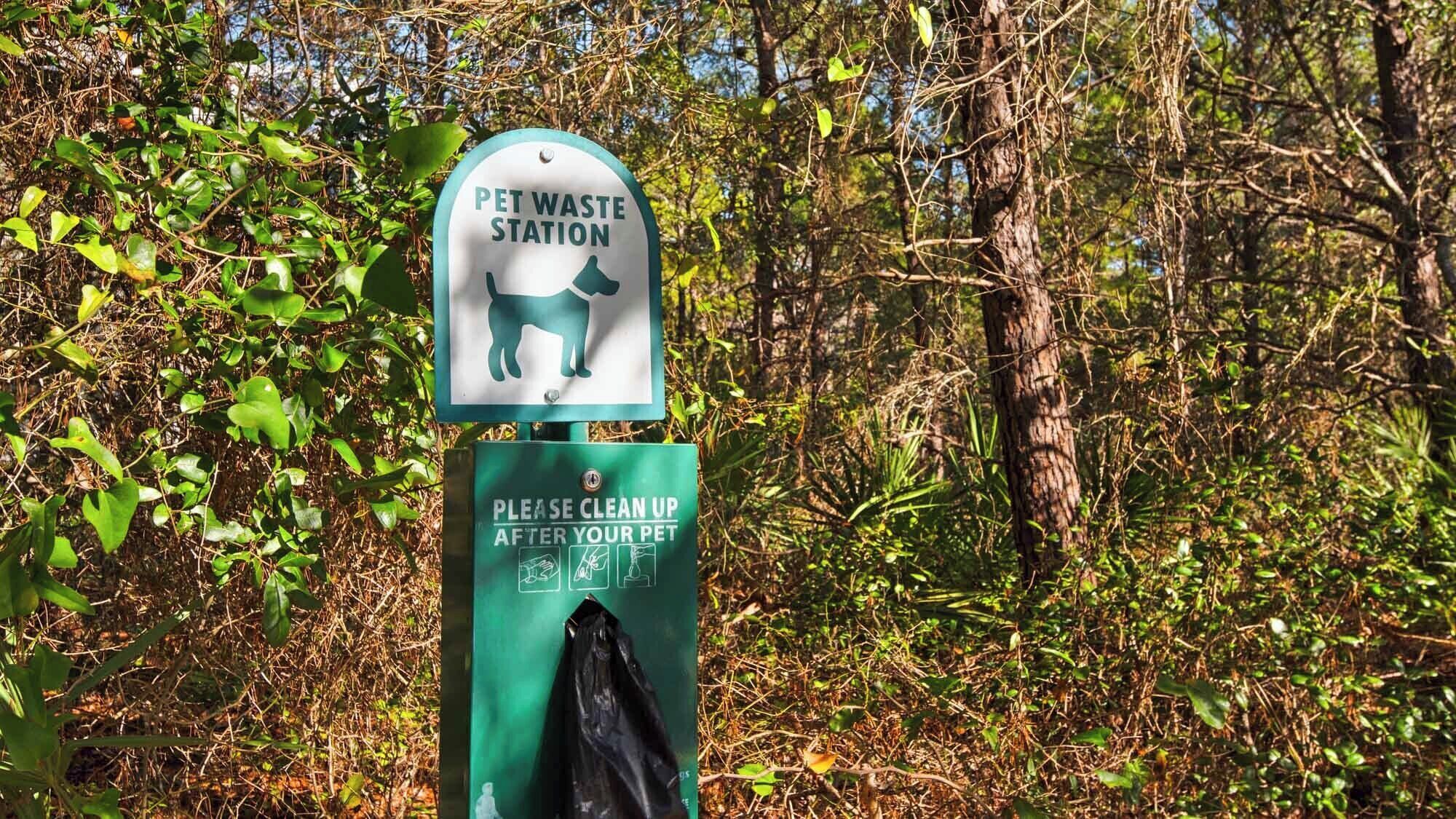 A pet waste station with a sign indicating it is a pet waste station and a request to clean up after your pet.