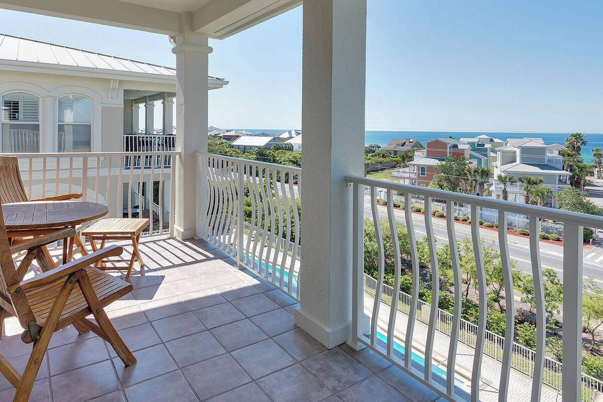A balcony with a table and chairs, a view of the ocean, and a pool.