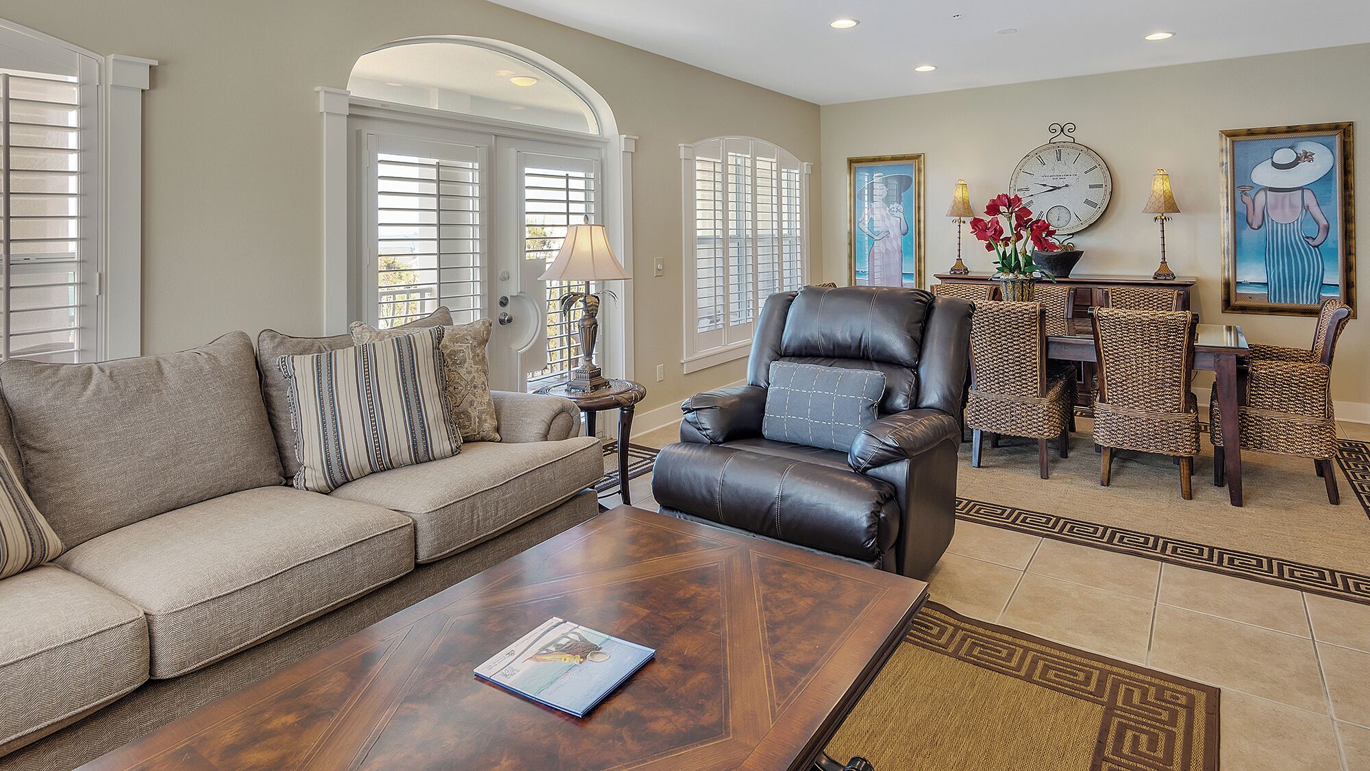 A living room with a leather armchair, a sofa, a coffee table, and a dining area with wicker chairs and a table.