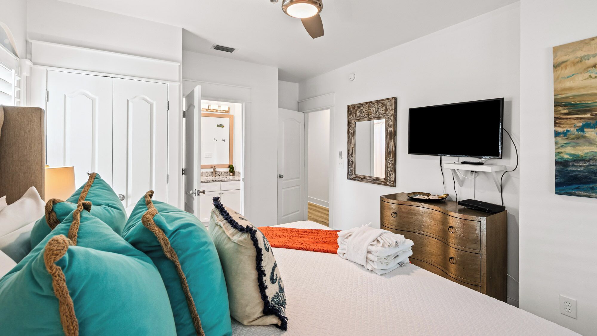 Une chambre à coucher avec un lit, une commode, un téléviseur et une salle de bain visible à travers une porte ouverte.