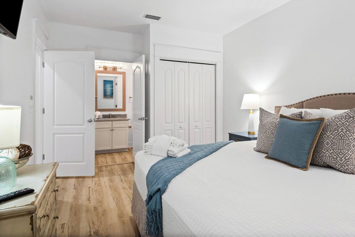 A hotel room with a bed, bedside table, lamp, and a view of the bathroom.