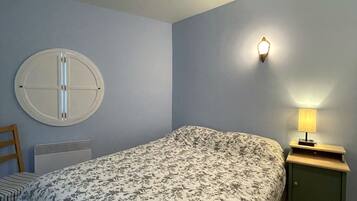 A bedroom with a bed, a nightstand with a lamp, a wall-mounted light, a radiator, and a round mirror.