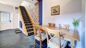 Un comedor con una mesa y sillas de madera, una escalera con pared de ladrillo y un cuadro en la pared.