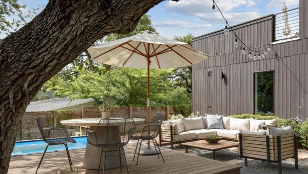 Eine Außenpatio mit Pool, einer Holzterrasse, einem Tisch mit Stühlen, einer Couch und einem Sonnenschirm.
