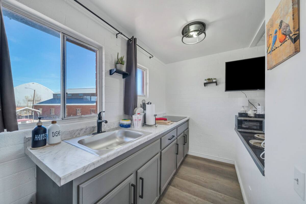 A modern kitchen with a large window, a built-in sink, and a flat-screen TV mounted on the wall.