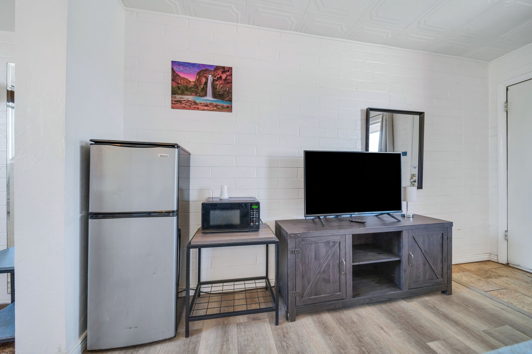 A kitchenette with a refrigerator, microwave, and a flat-screen TV on a wooden cabinet.